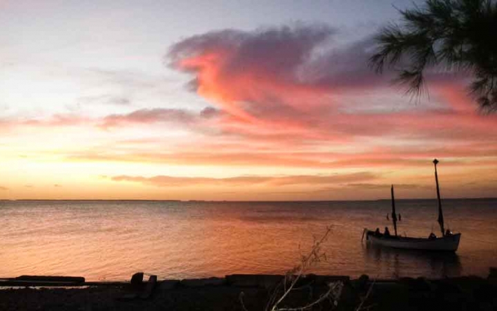 a sailboat floats in calm water at sunset